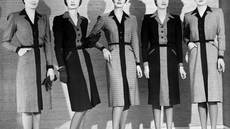 A black and white photograph of five women wearing suit dresses.