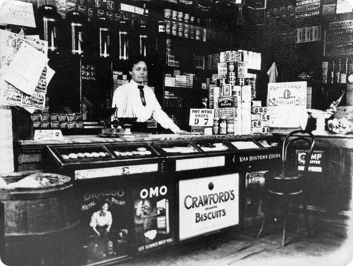 A woman behind the counter of a general store. Cambridge, circa 1920.