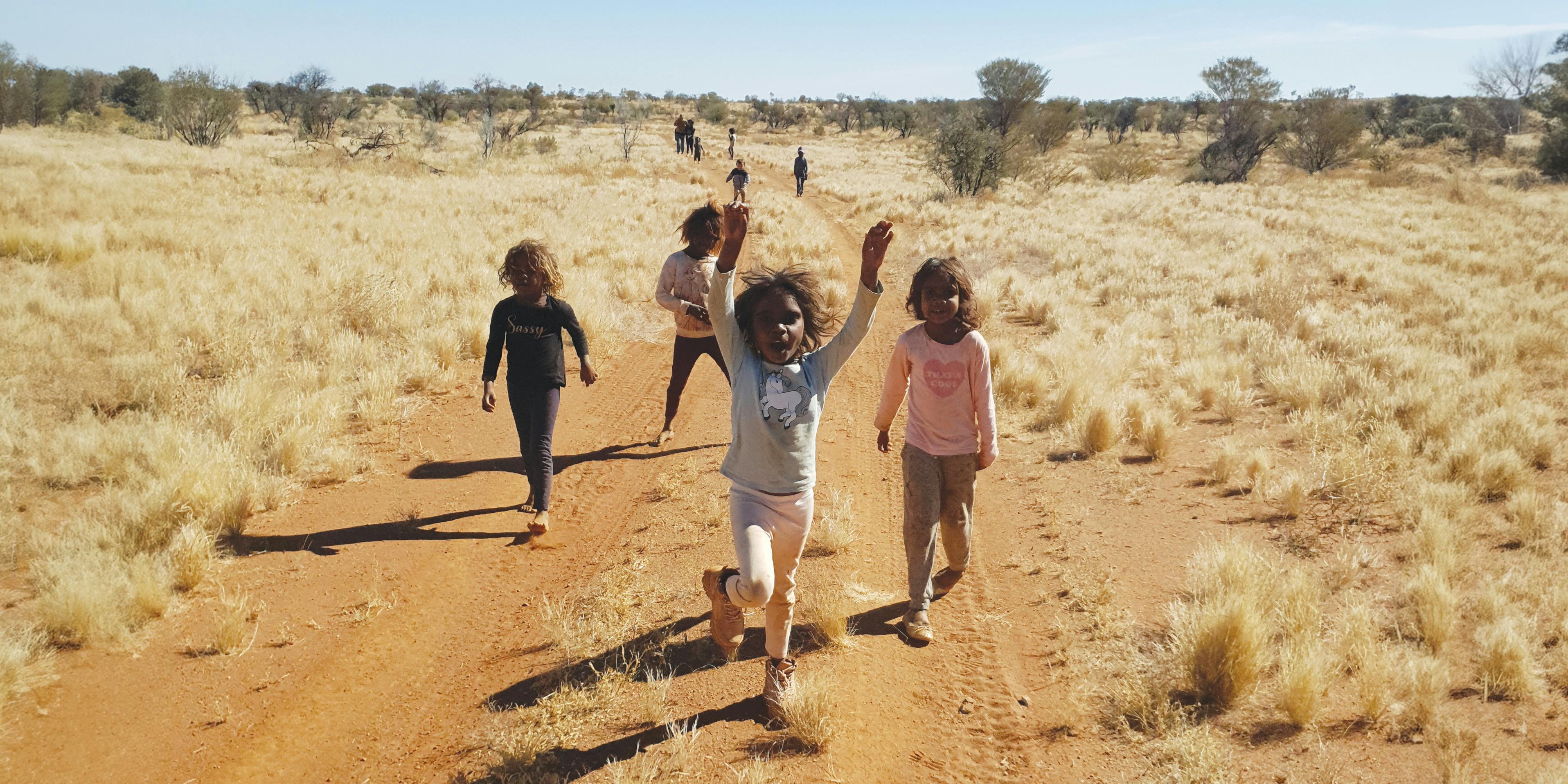 A group of Indigenous children walking on a dirt path road through the desert.