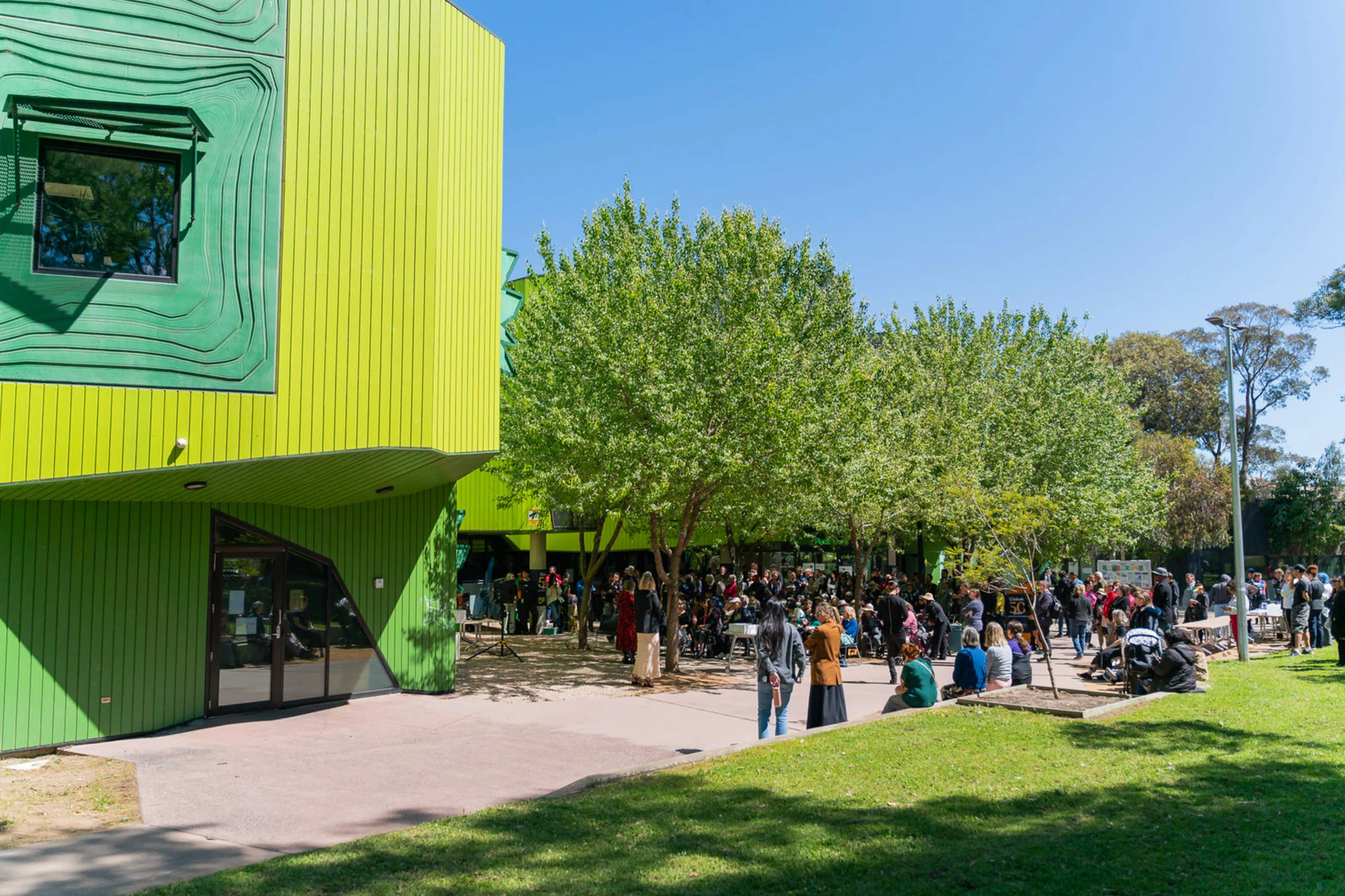 North Richmond Community Health Centre enveloped by a crowd of people and two large trees.