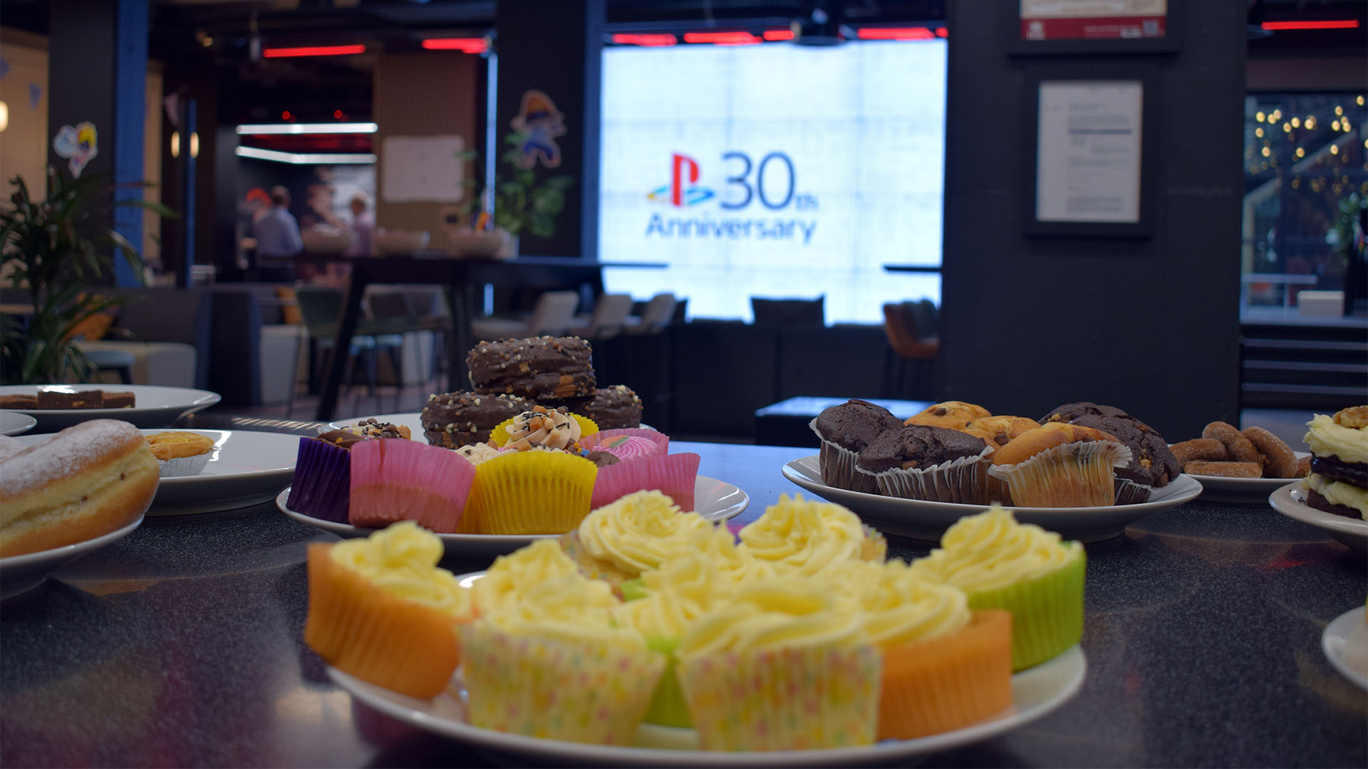 A close-up of a desk scene in an office, with a table full of cakes and cupcakes. 