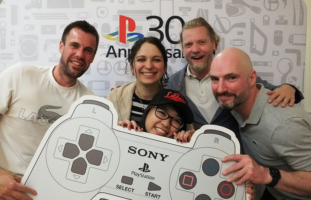5 sprites holding a PlayStation 1 controller cut out posing for a team photograph