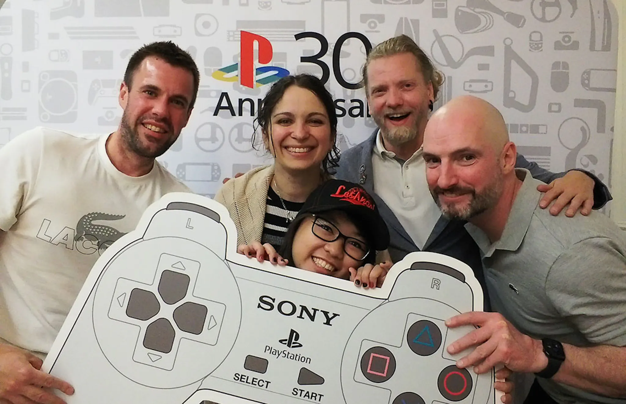 5 sprites holding a PlayStation 1 controller cut out posing for a team photograph