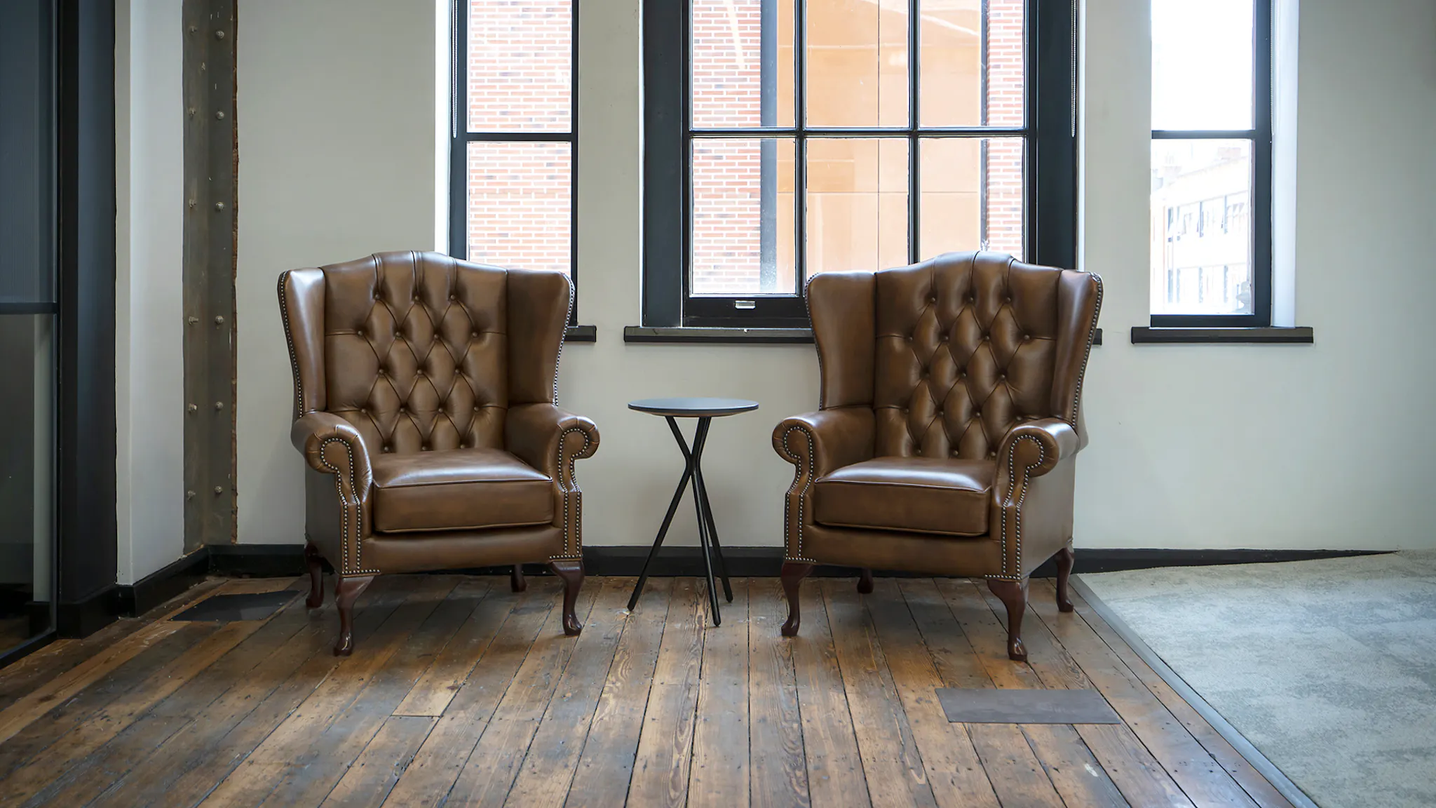 Two chairs on a wooden floor in a quiet office room. A single soft blub lights the space, the white walls and surrounding plant life.