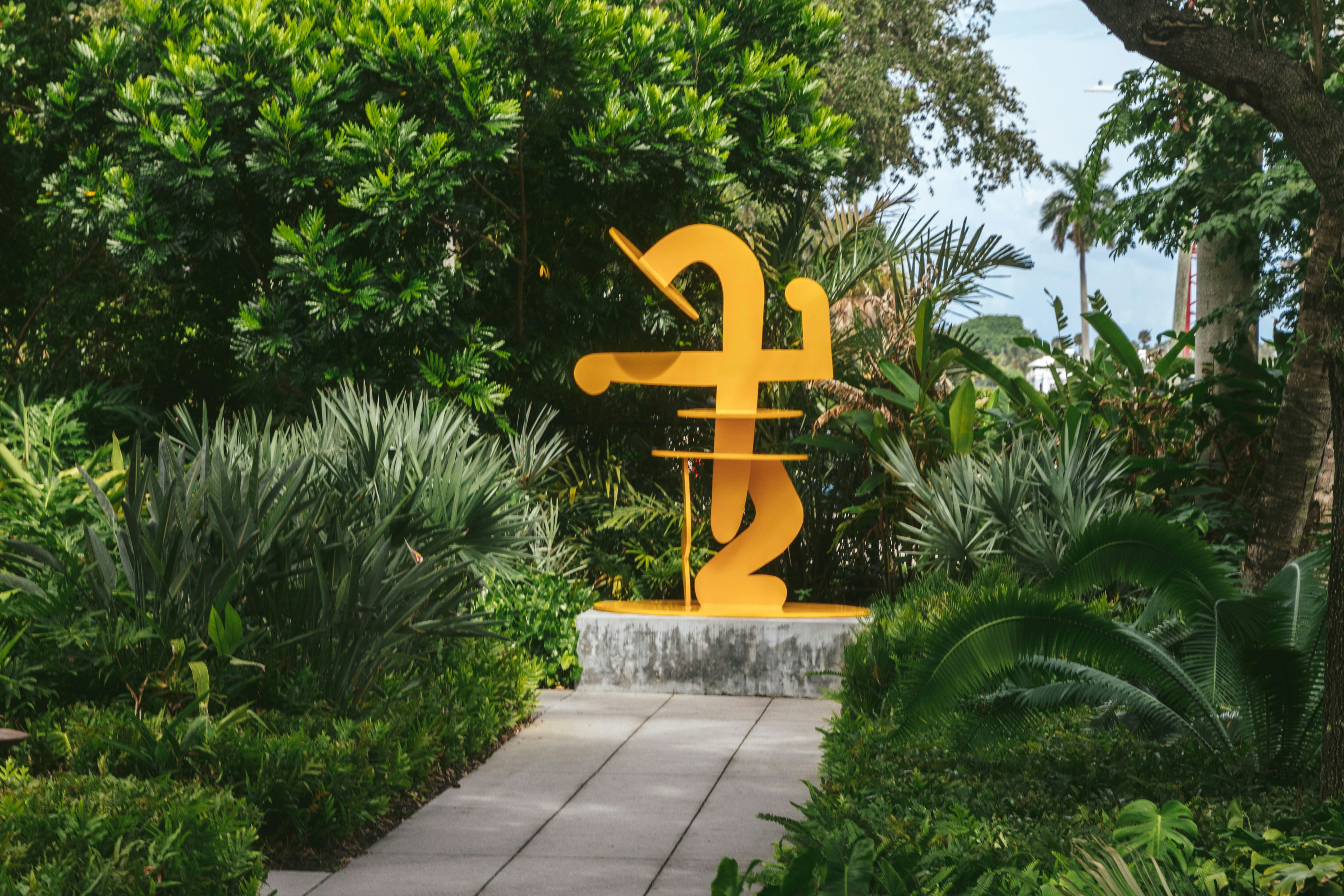 Outdoor orange art exhibit at the end of a walkway surrounded by green plants.