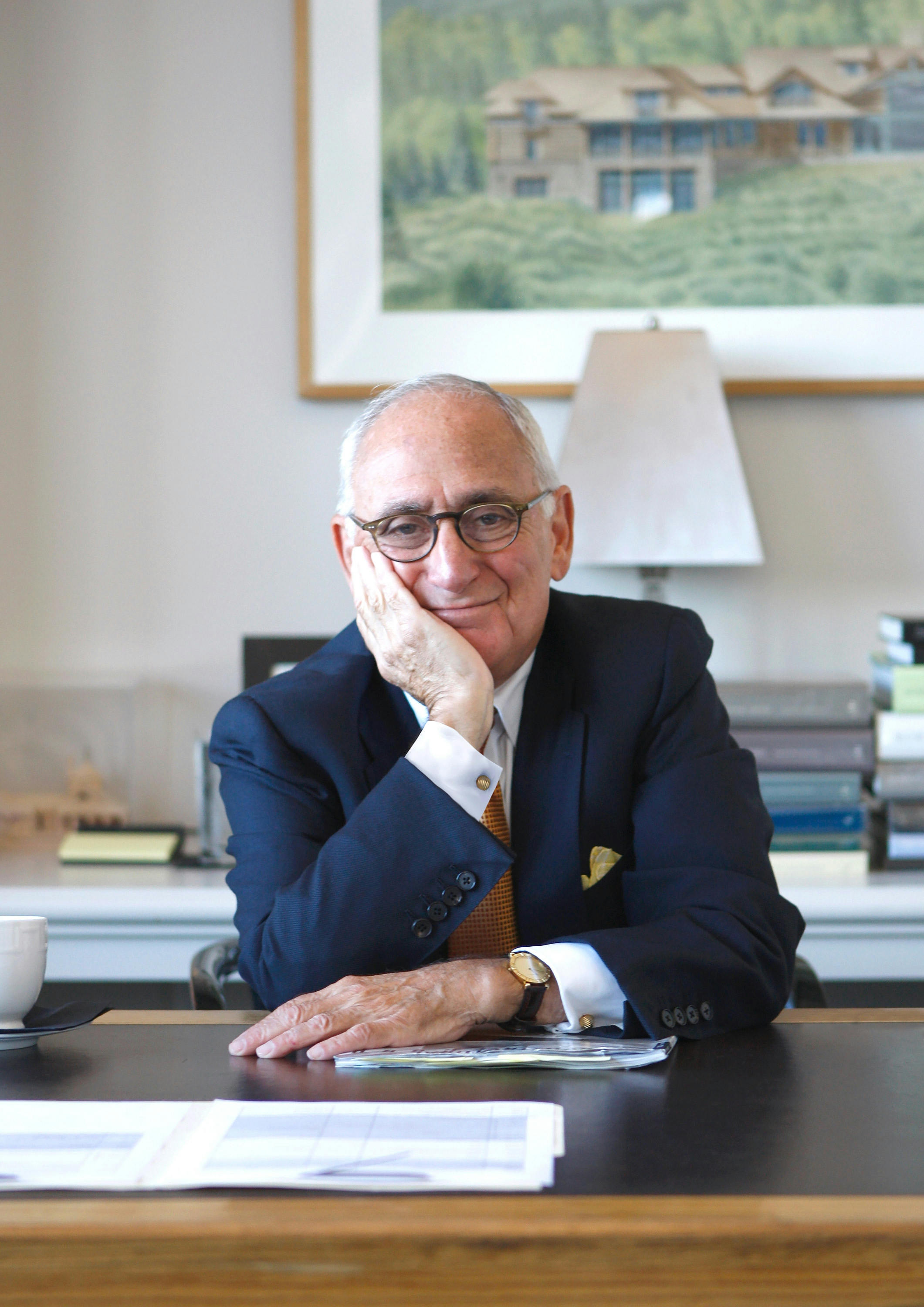Robert A.M. Stern sitting at a desk leaning on one arm in a navy suit.