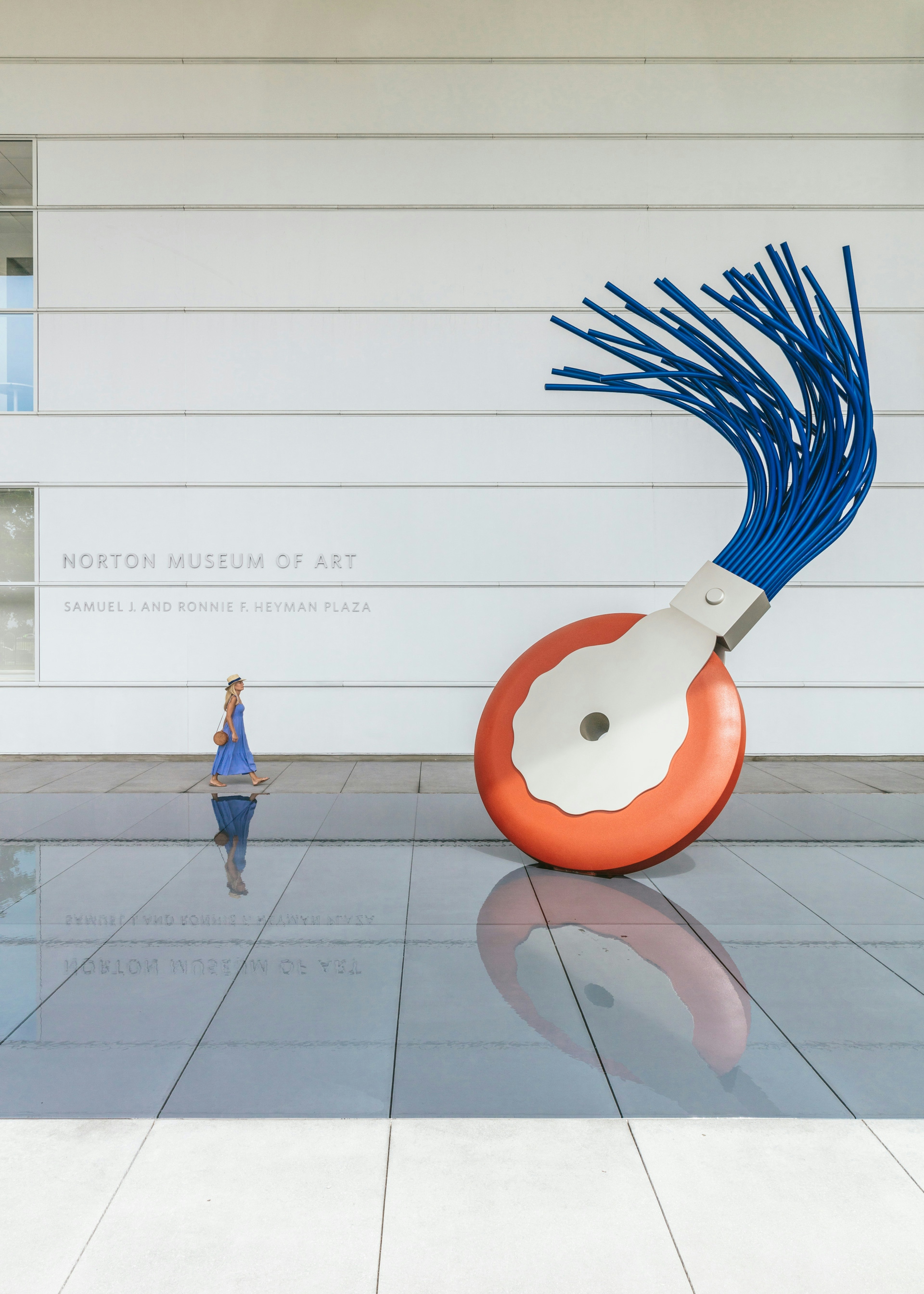 Person walking near an outdoor art exhibit at Norton Museum of Art in Samuel J. and Ronnie F. Heyman Plaza.
