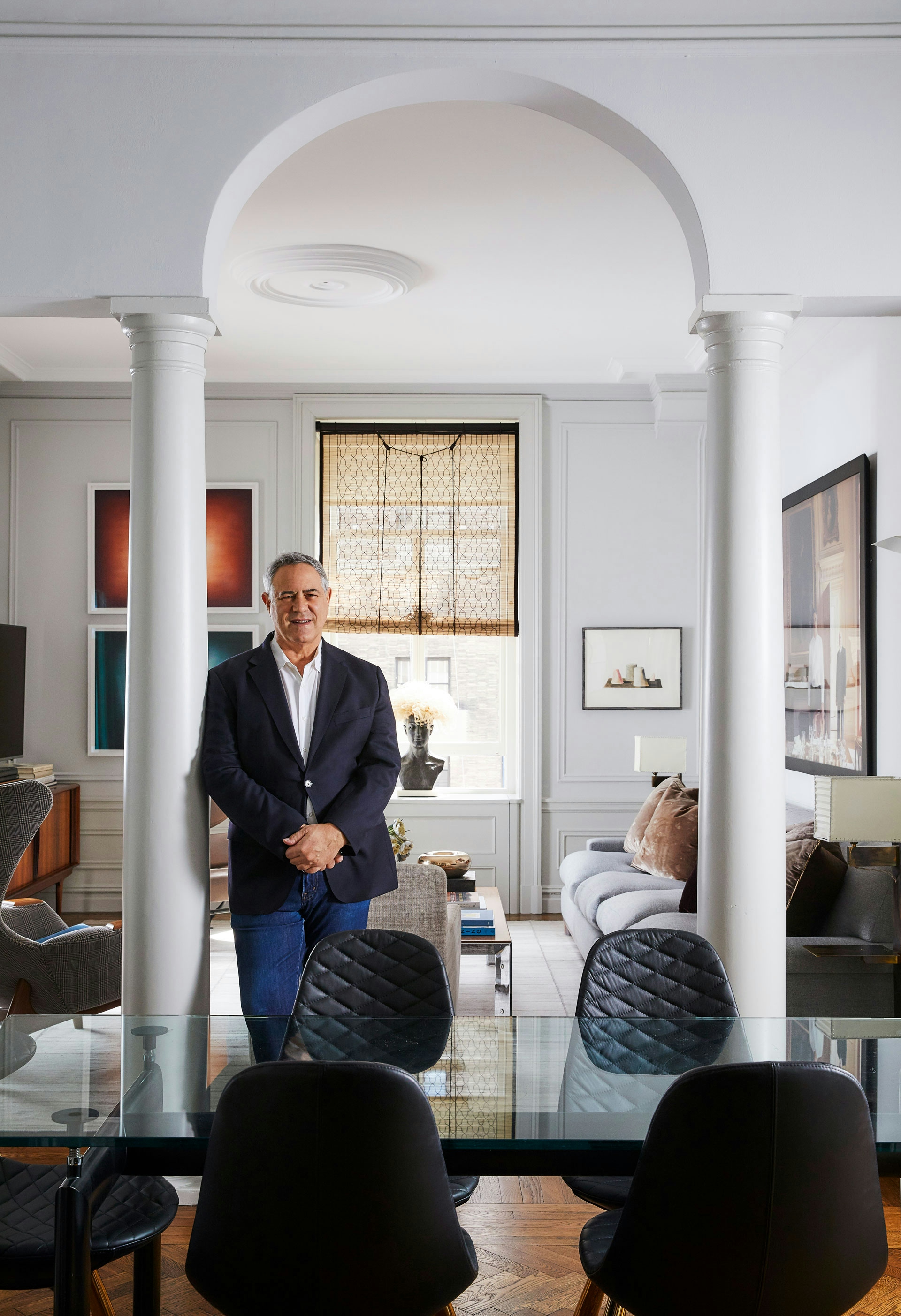 Andrew Sheinman leaning on a pillar, wearing a suit in an open living and dining area.
