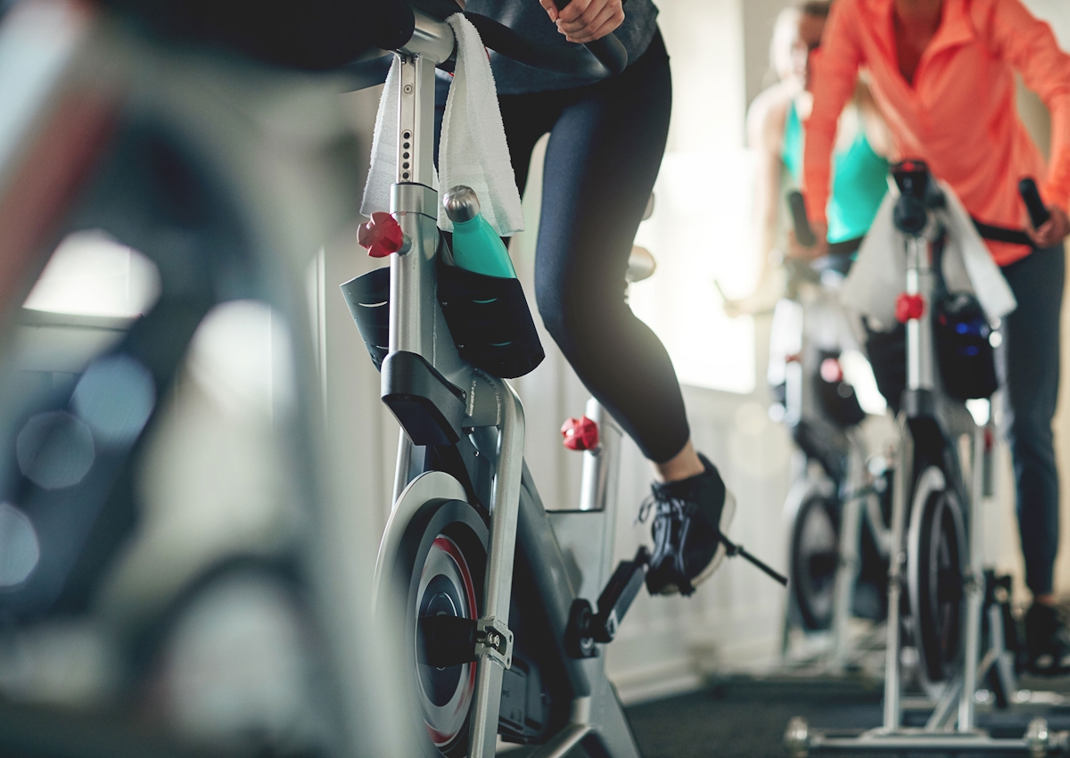 Workout class with people in fitness attire on stationary bikes in a sun-filled room.