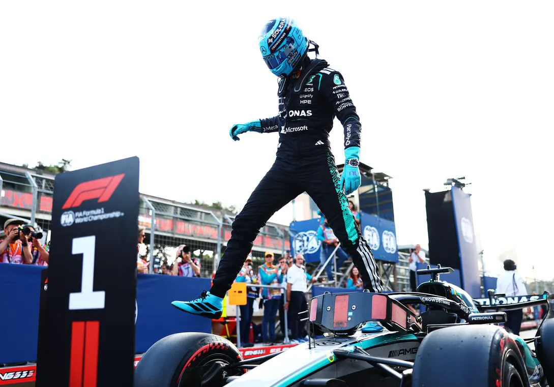 An F1 racer in full gear and helmet steps over the car.