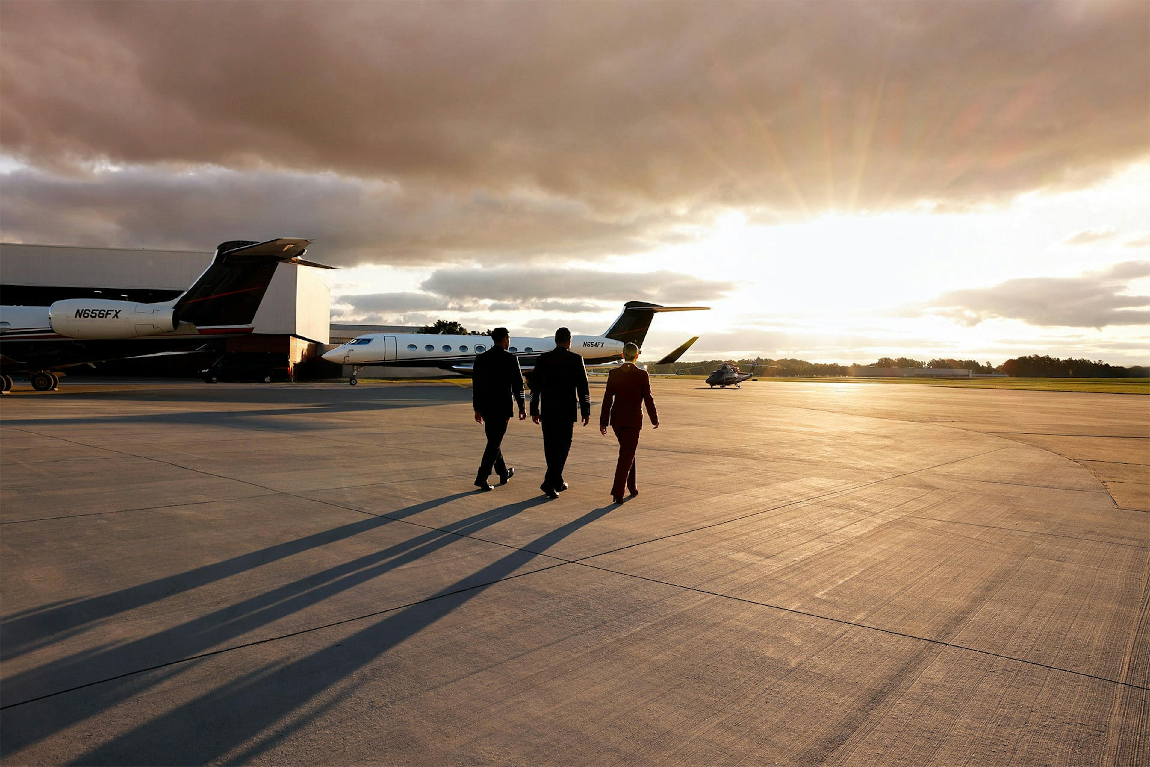 Three flight crew members walk towards an aircraft in the golden sunset