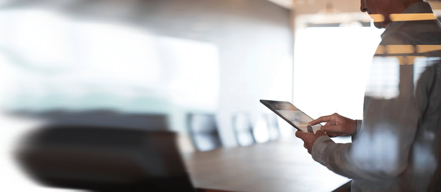Someone uses a tablet focused with a blurred board room in the background