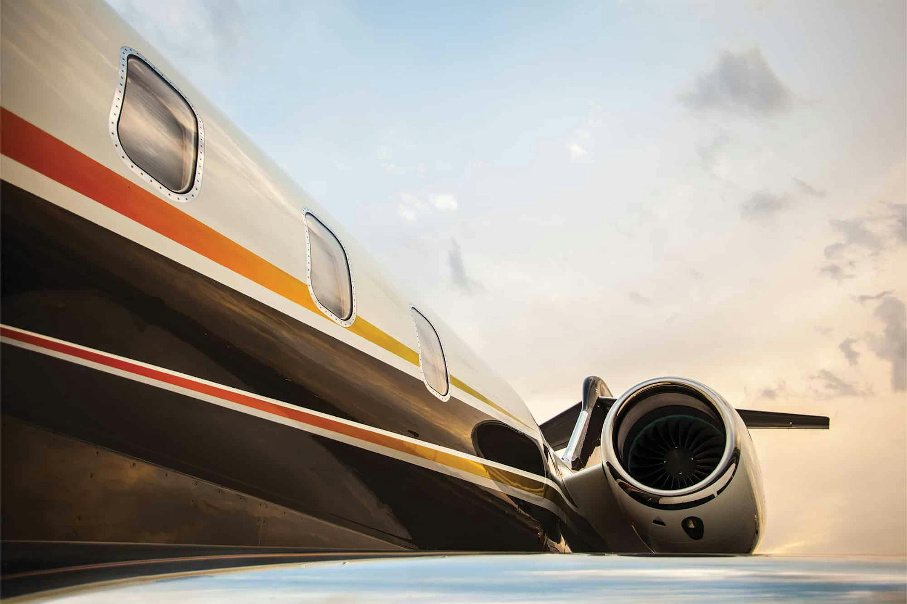 side view of the exterior of a flexjet aircraft from the wing, light clouds and blue skies behind it