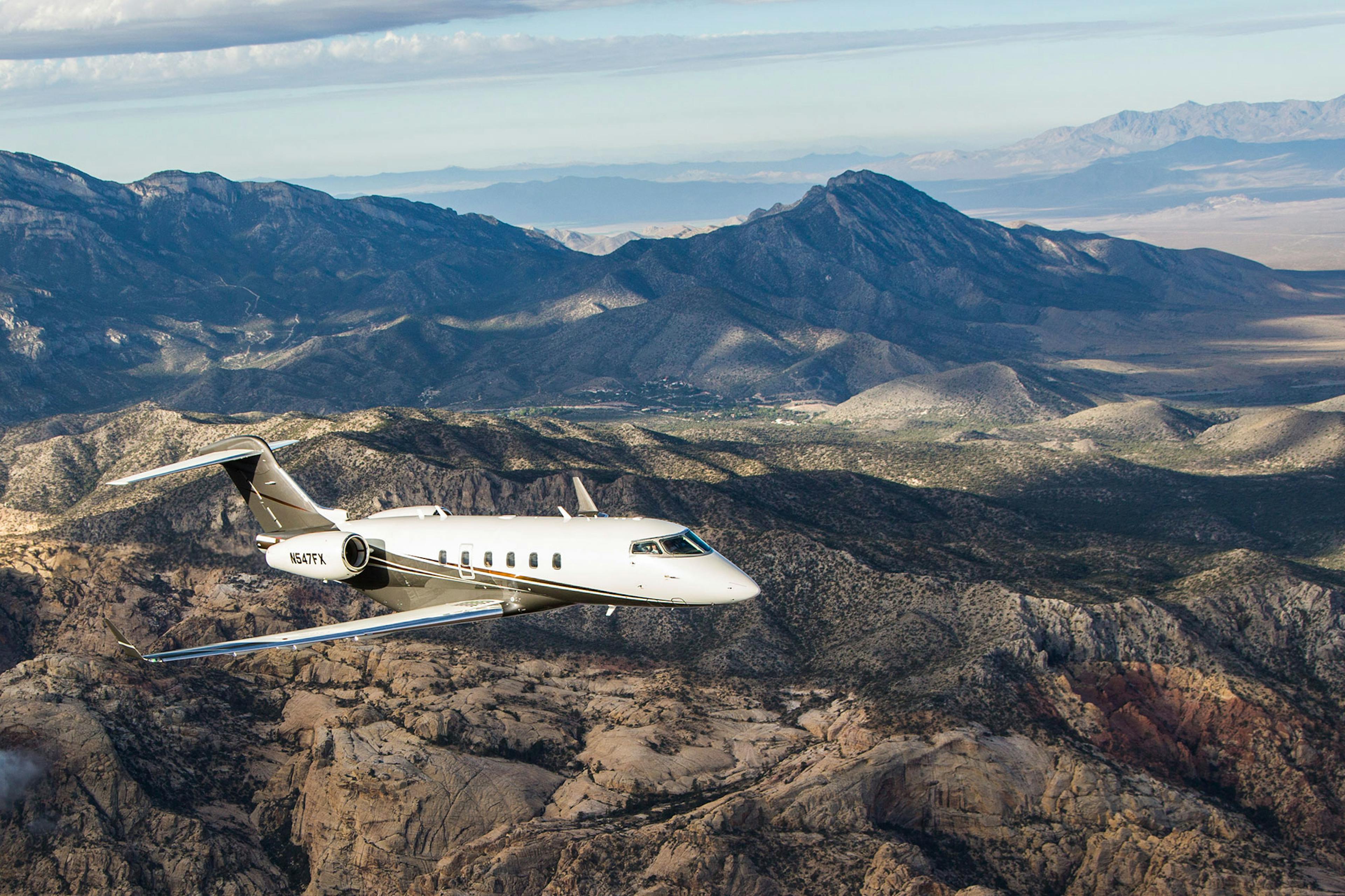 A flexjet aircraft is flying over desert mountains speckled with green trees