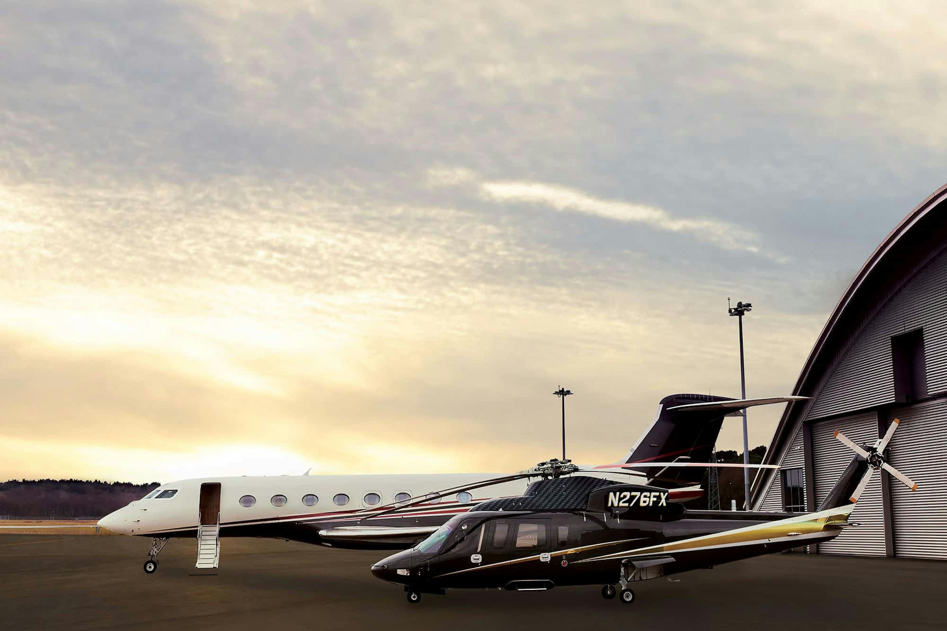An s76 and flexjet fixed wing sits on the tarmac with the sun setting