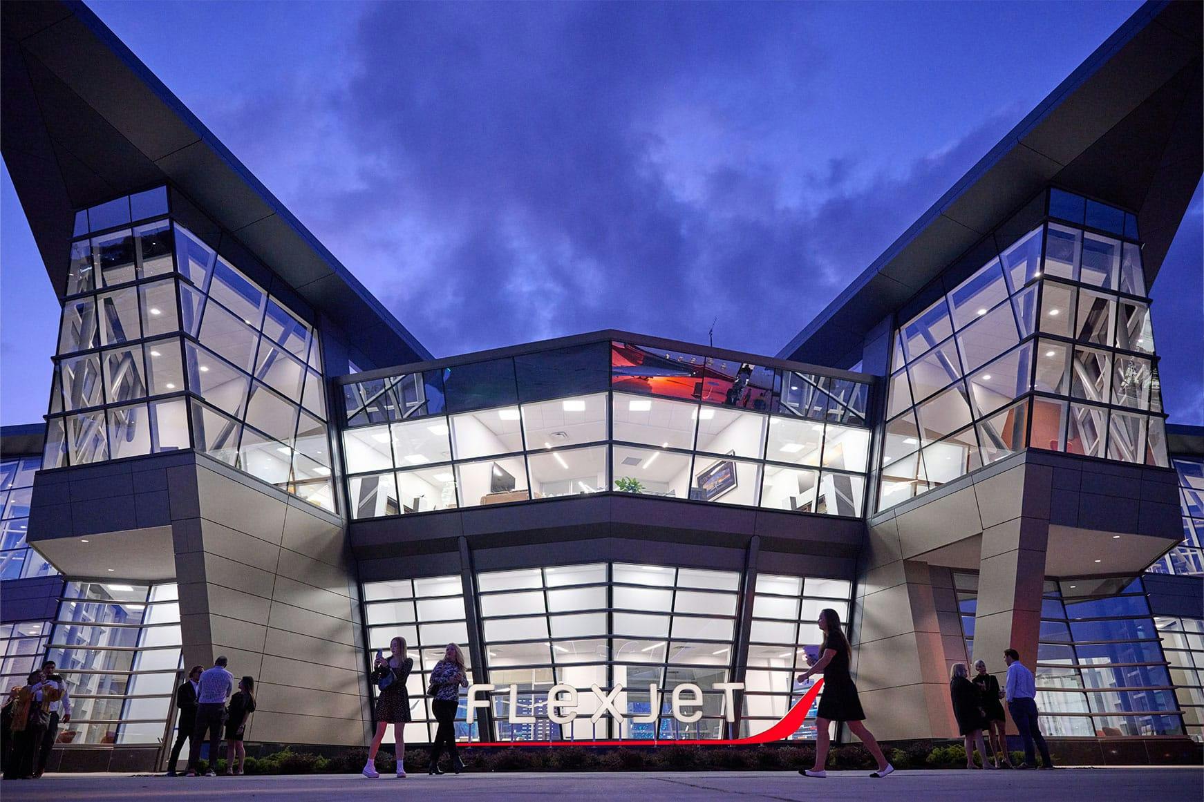 Flexjet Headquarters building illuminated with dark skies behind and people gathering and walking out front