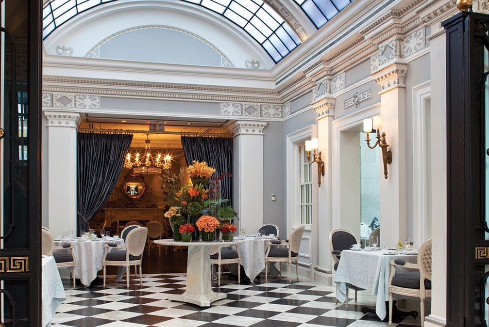 Checkered tile and white chairs and tables with colorful flowers within an atrium