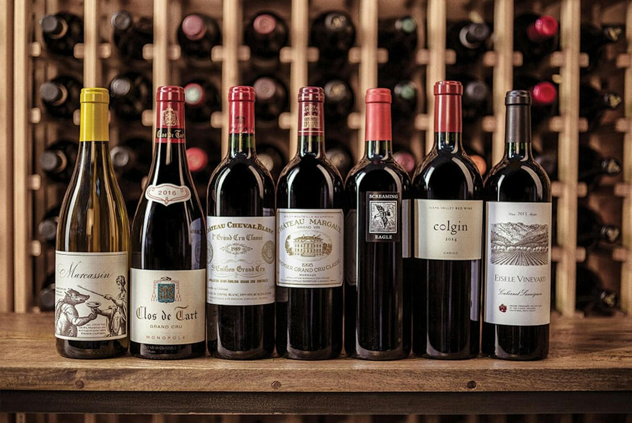 a row of fancy wine bottles, labels facing out, bottles stacked up in the background