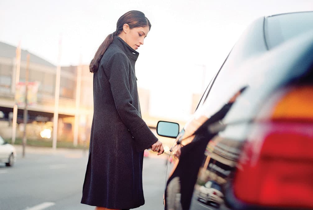 a woman inputs her key into the driver side door of her car