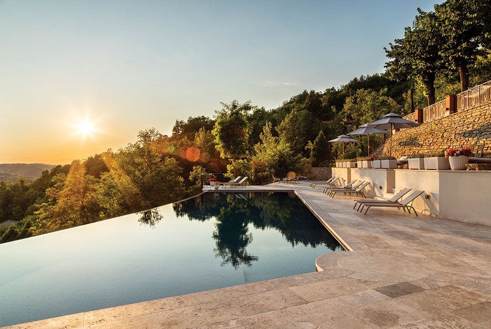 Glasslike waters of an infinity pool on the hill with a sun setting in the sky