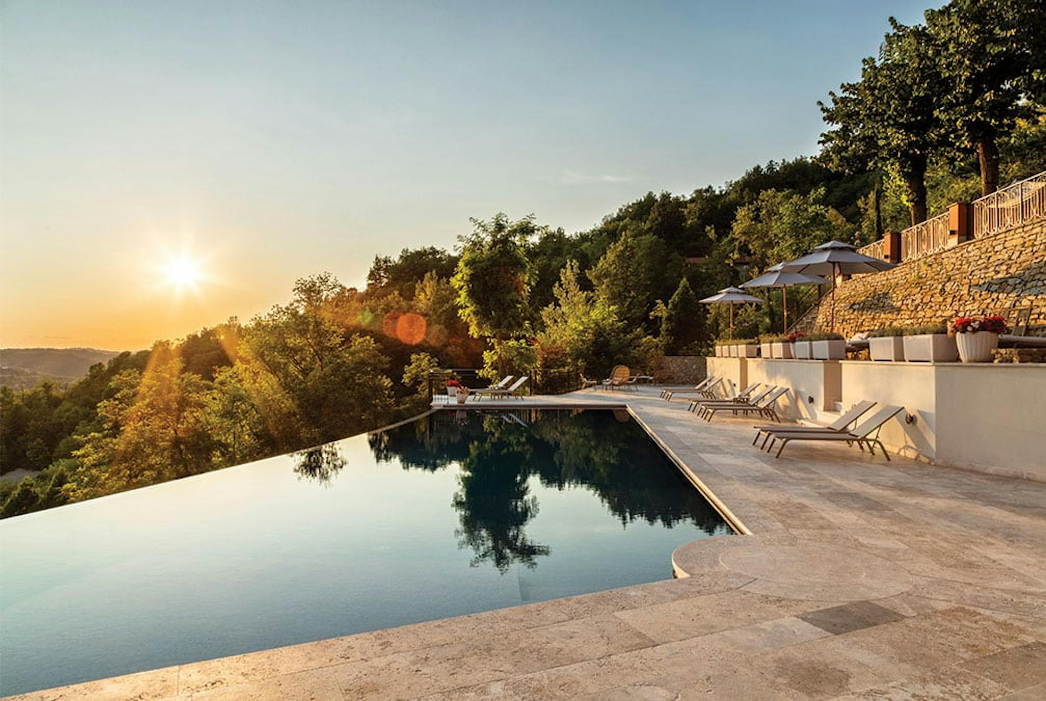 Glasslike waters of an infinity pool on the hill with a sun setting in the sky