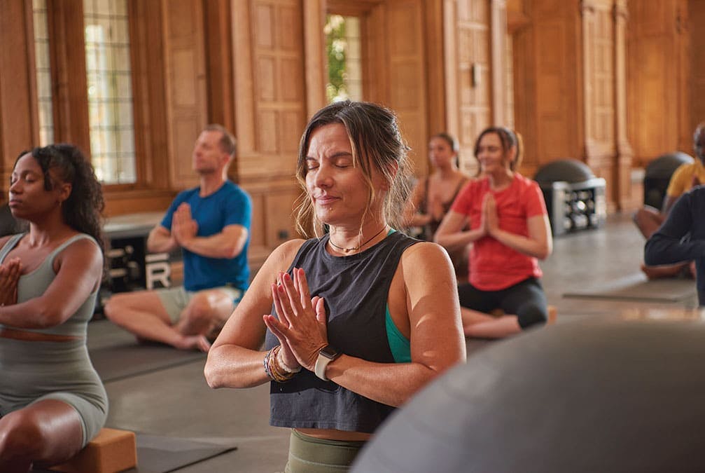 A yoga session focuses on a woman with hands together and eyes closed