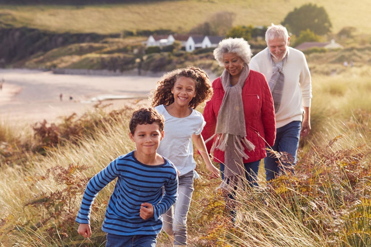 Kids running happily on a trail through grass fields with grandparents close behind