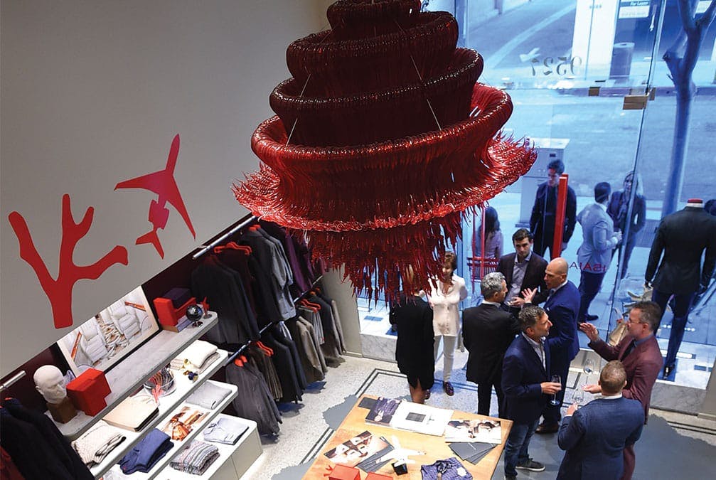 Ornate chandelier of red and tassels hangs over many people conversing at a boutique shop