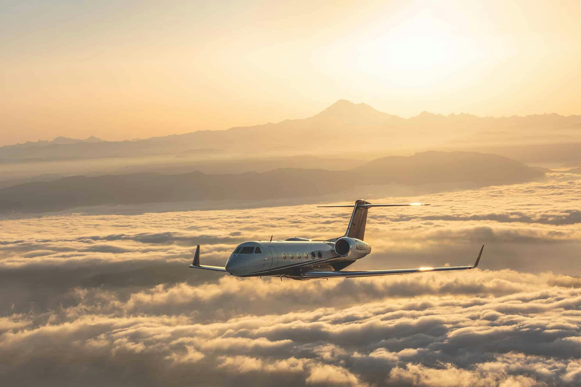 Yellowy sun light on the horizon tails a flexjet aircraft flying over the clouds