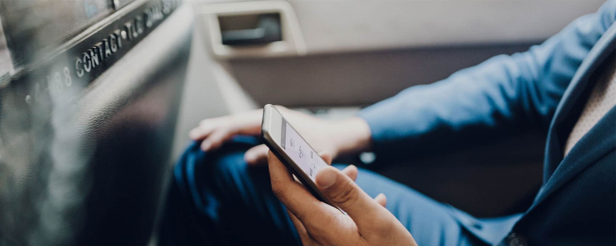 Someone sits look at their phone in one hand with the other resting on his knee