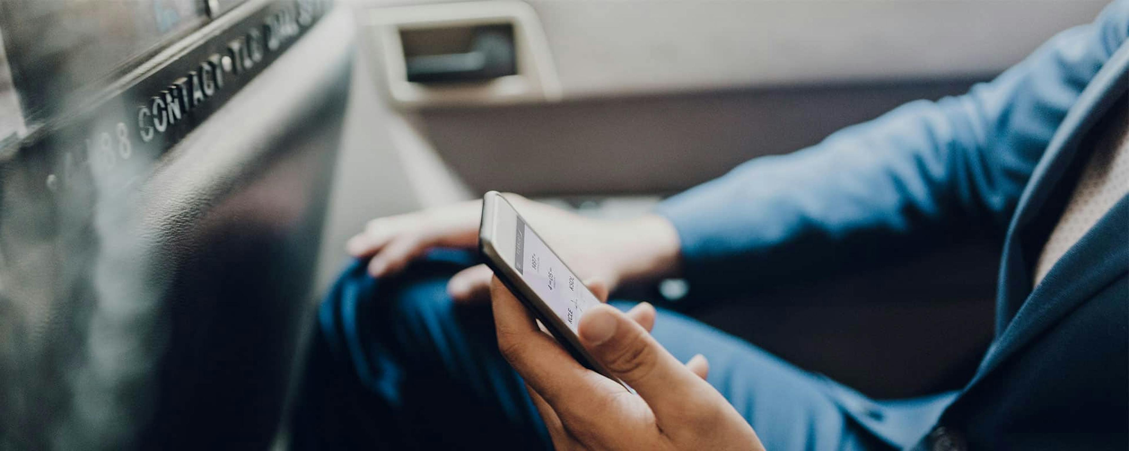 Someone sits look at their phone in one hand with the other resting on his knee