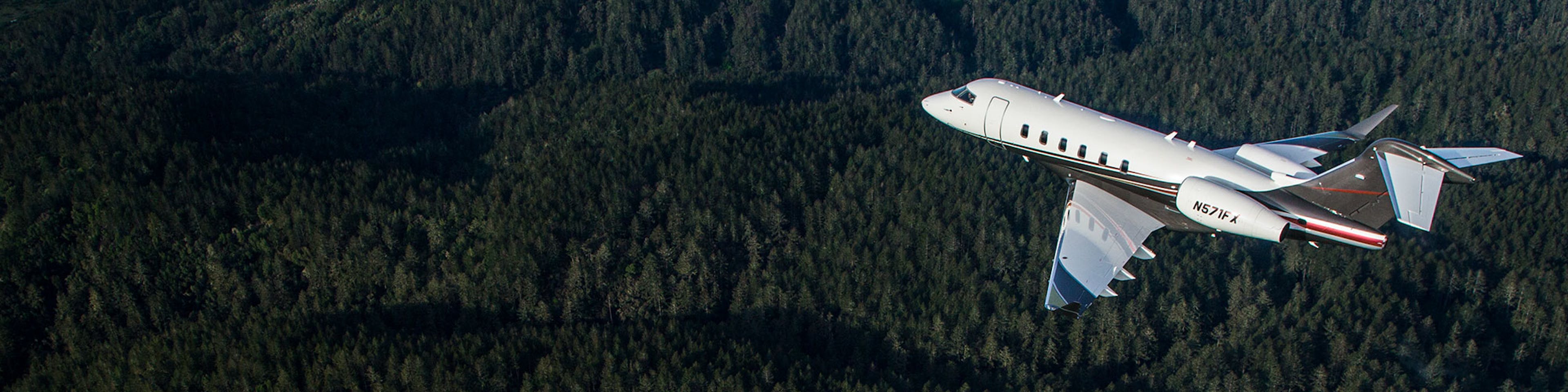 A flexjet aircraft flies over tree covered mountains