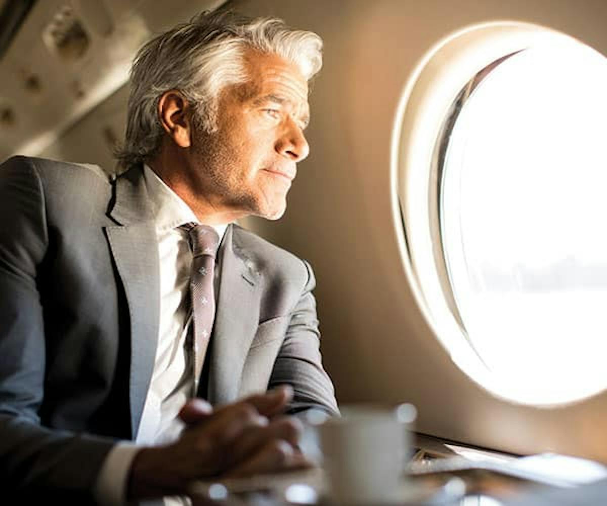 A man in a suit stares out the rounded window of a private jet