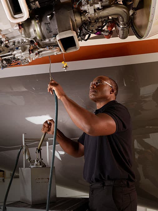 A man holds up some equipment as he inspects the exposed components of an aircraft