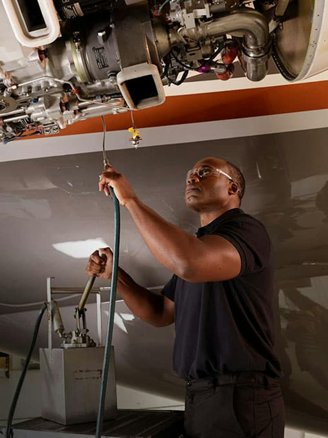 A man holds up some equipment as he inspects the exposed components of an aircraft