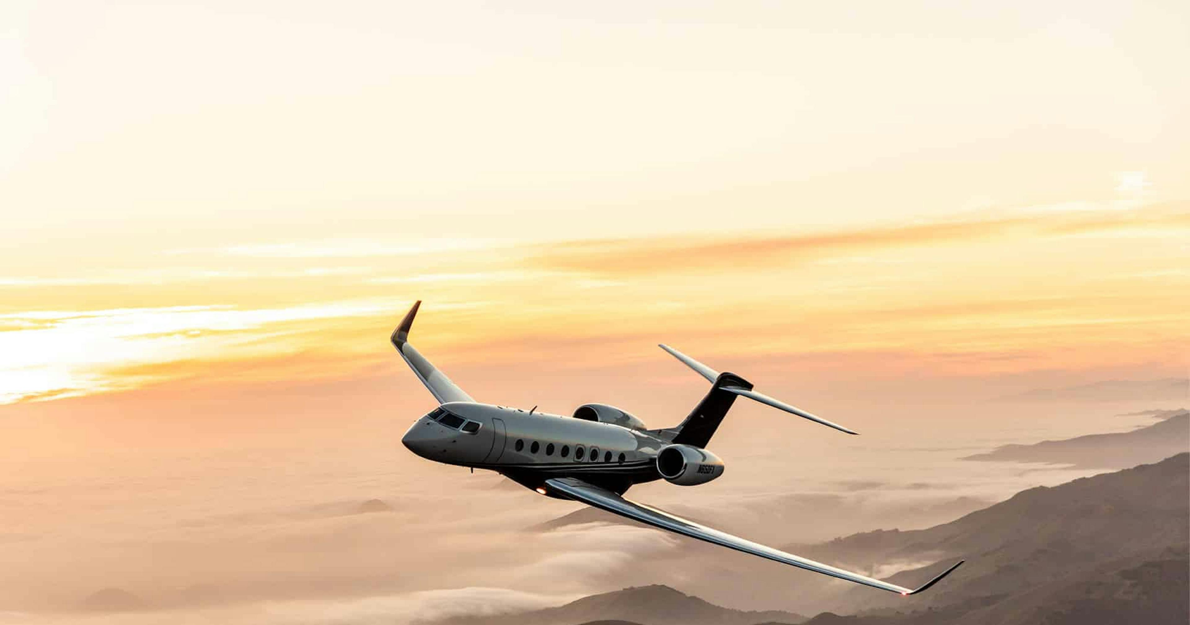 A plane tilts slightly left flying over rolling mountains above clouds illuminated by the sunlight