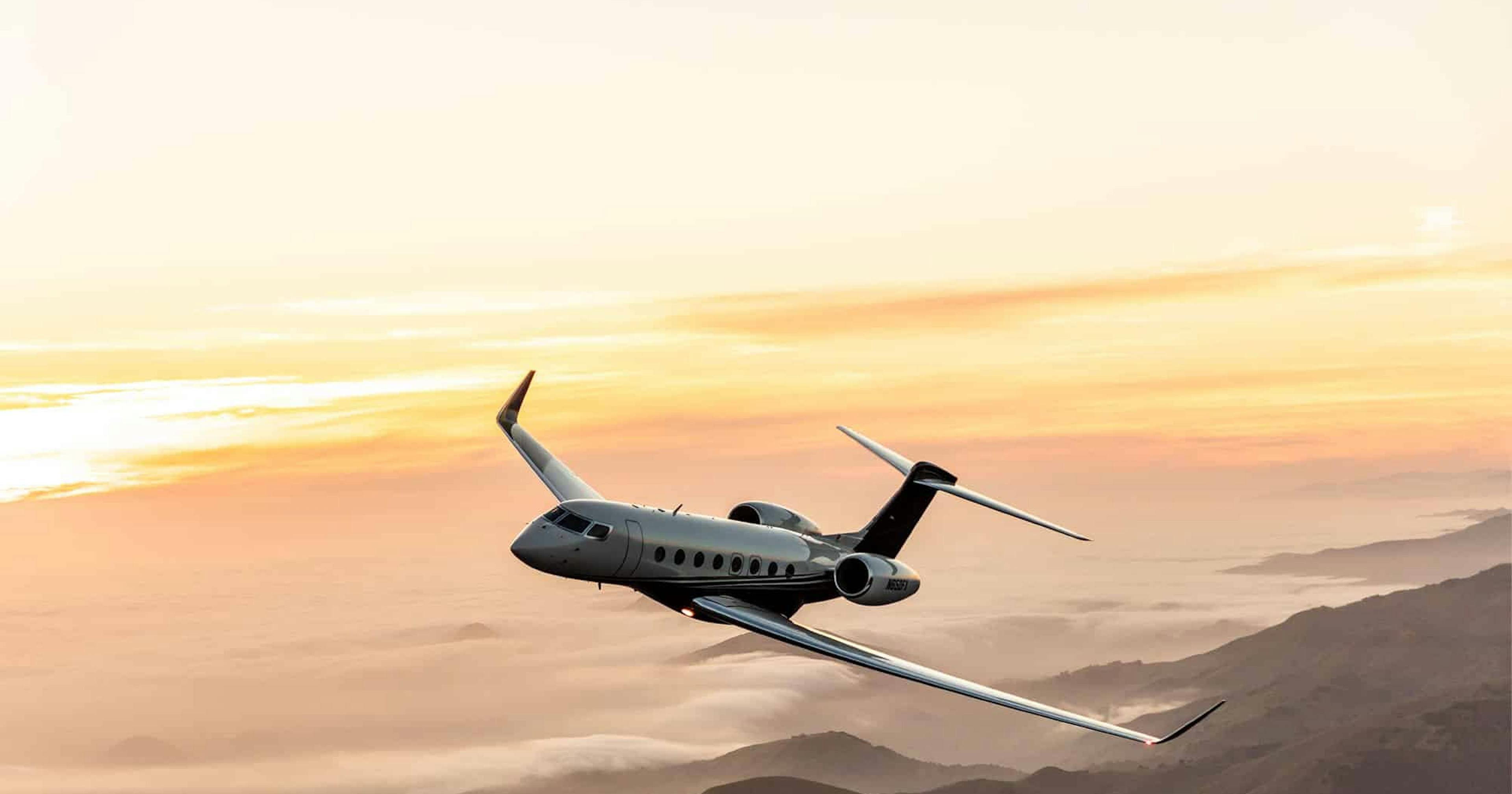 A plane tilts slightly left flying over rolling mountains above clouds illuminated by the sunlight