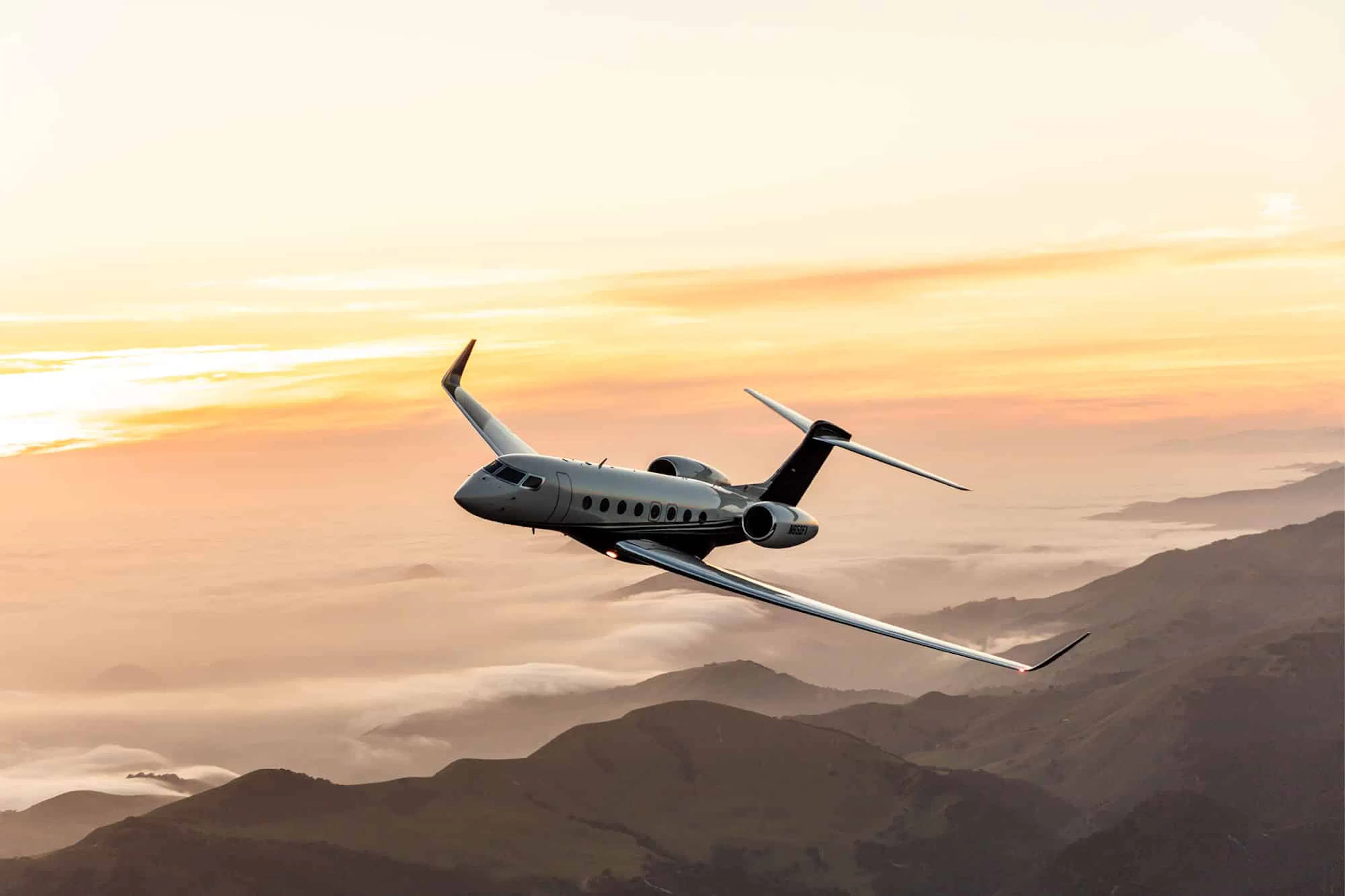A plane tilts slightly left flying over rolling mountains above clouds illuminated by the sunlight