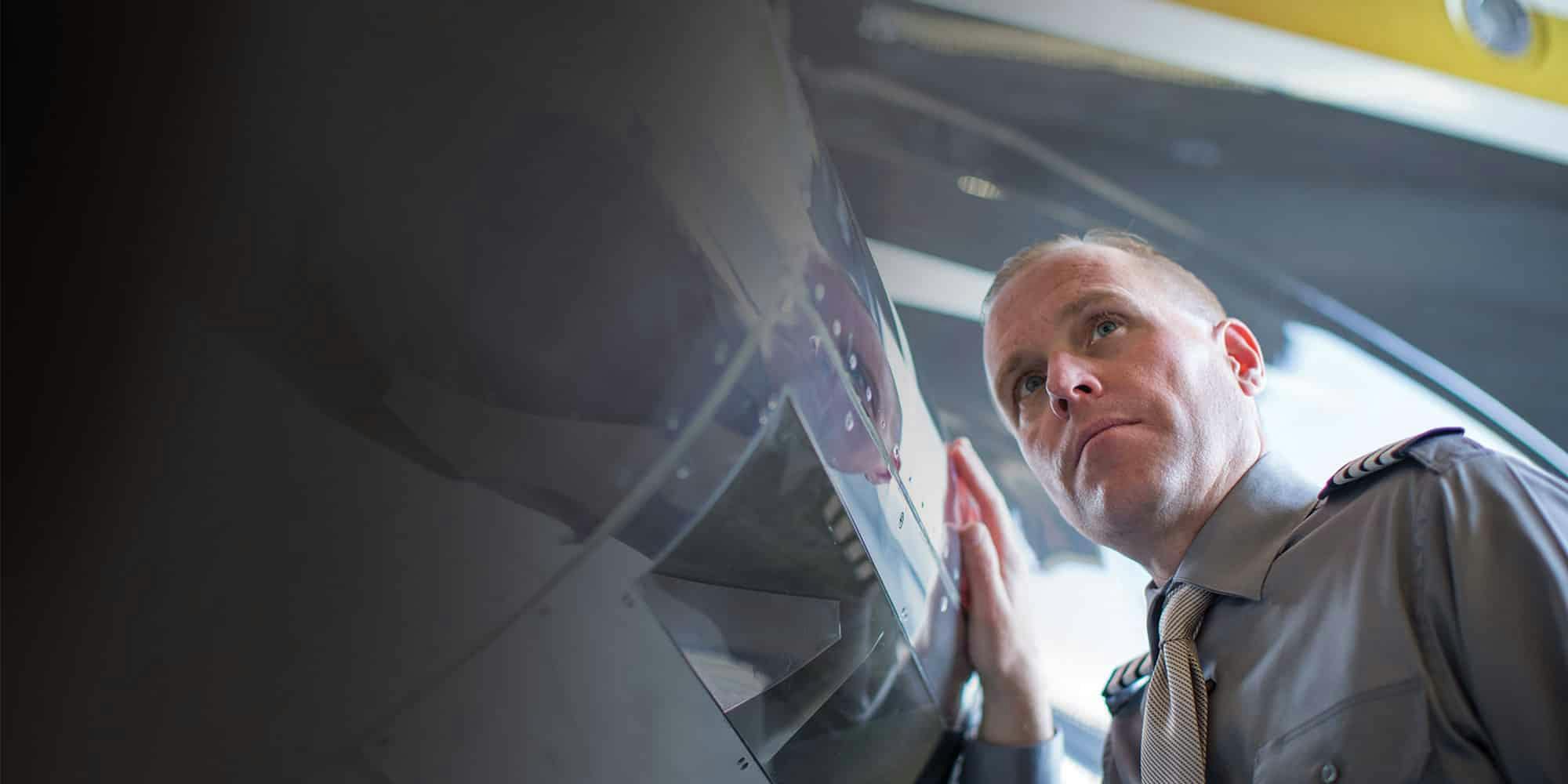 A man with a serious expression closely inspects the exterior of an aircraft