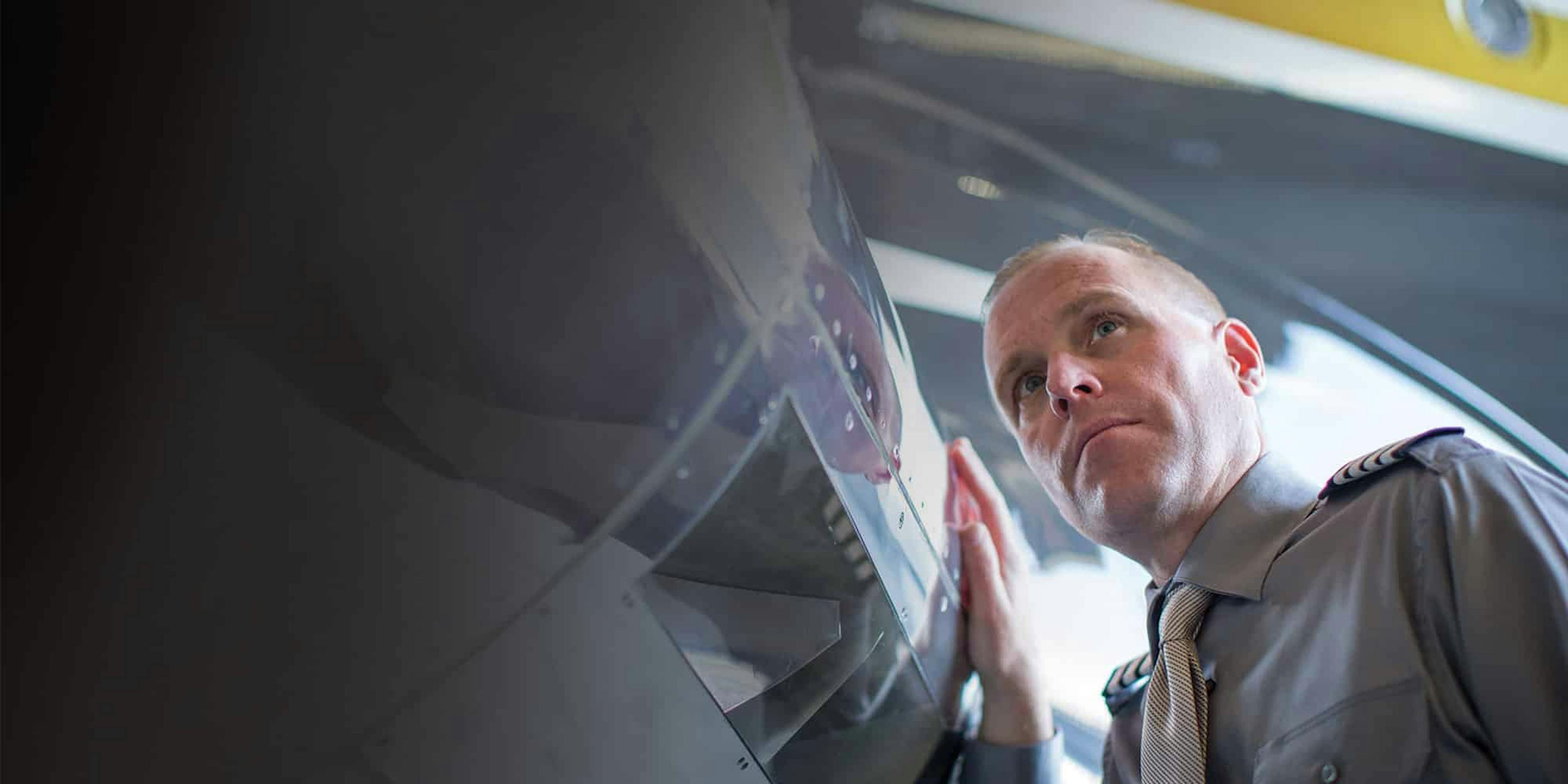 A man with a serious expression closely inspects the exterior of an aircraft