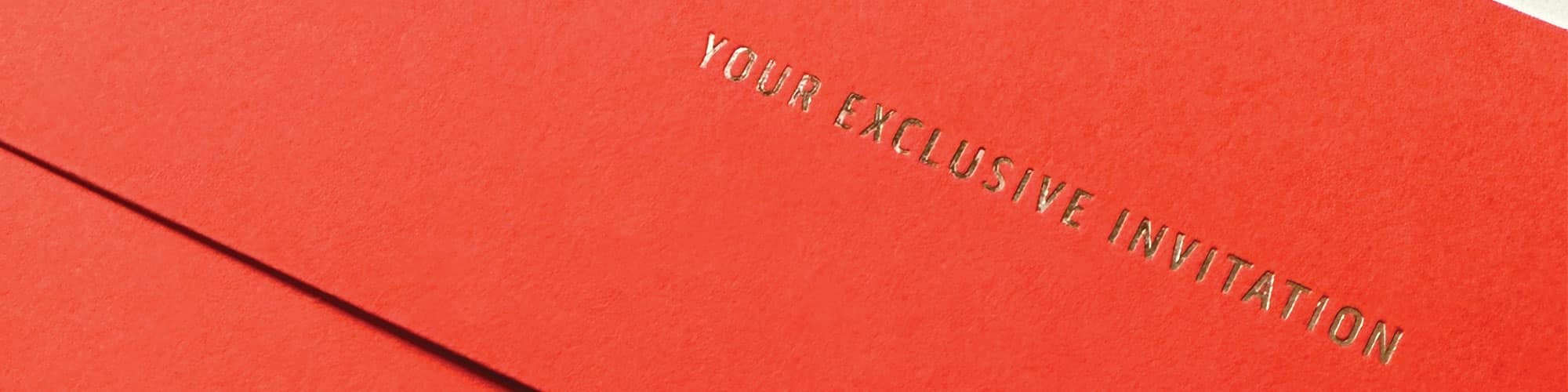 Close up of orangish red paper with the gold-pressed words Your Exclusive Invite