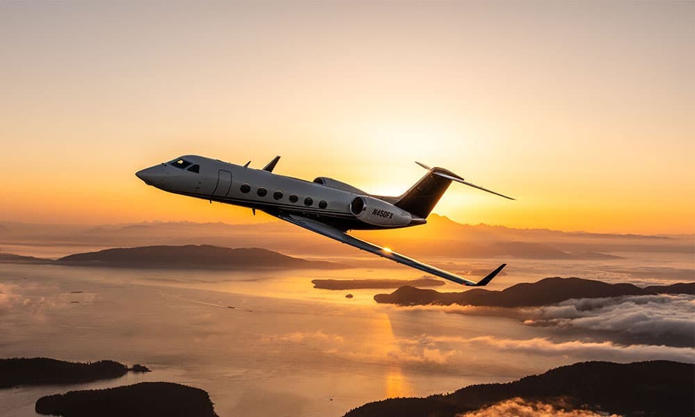 G450 flies over yellow sunset shining on glossy waters and rocky inlets