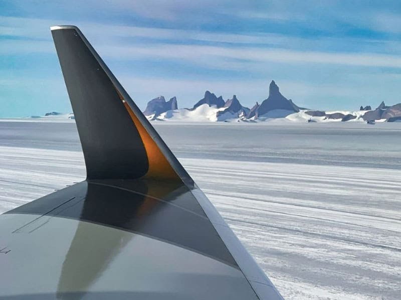 A wing with an icy runway and snow covered craggy mountains in the distance