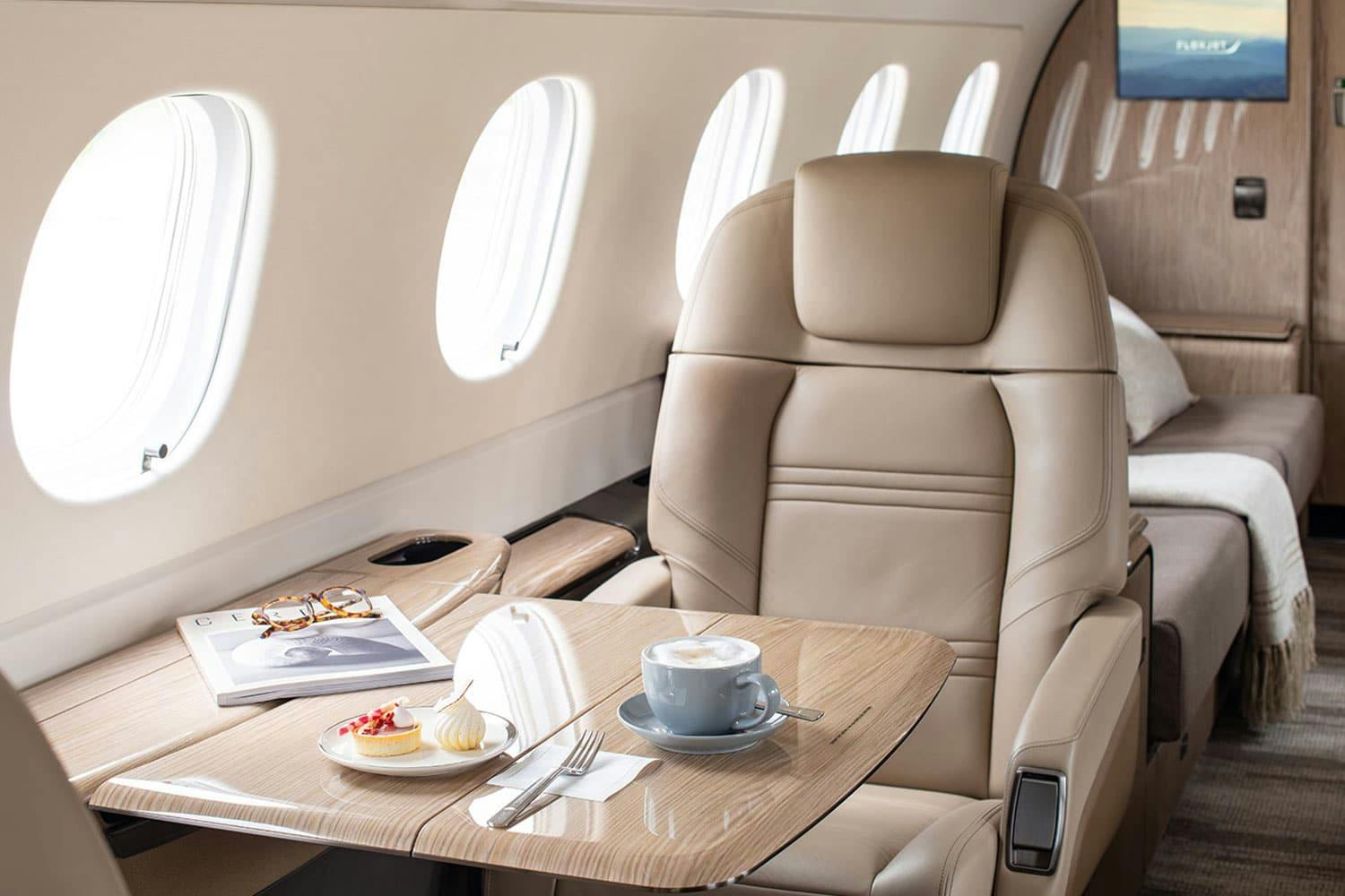 a magazine, some food on a plate, and a cup of latte or coffee sits on a table extended from a window in a plane