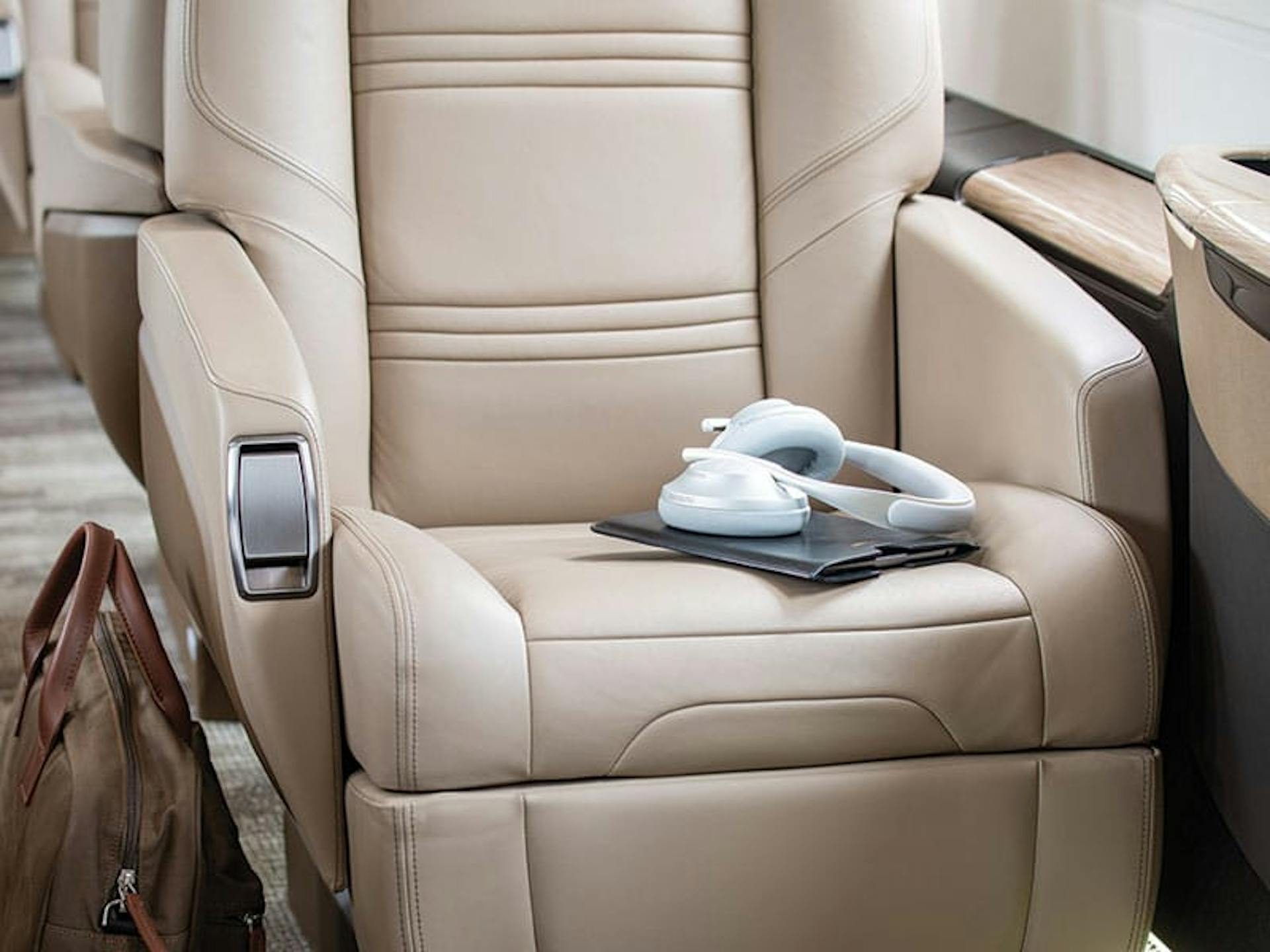 Inside the Praetor 500, this photo is zoomed in on one particular seat that has some headphones and a tablet and protective case on top of it and brown swede bag on the floor next to it. 