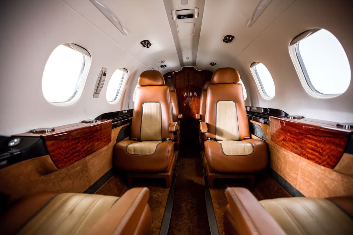 Quality interior of the Phenom 300, focused on the middle of the cabin with custom seating and carpet, cabinets and side tables.