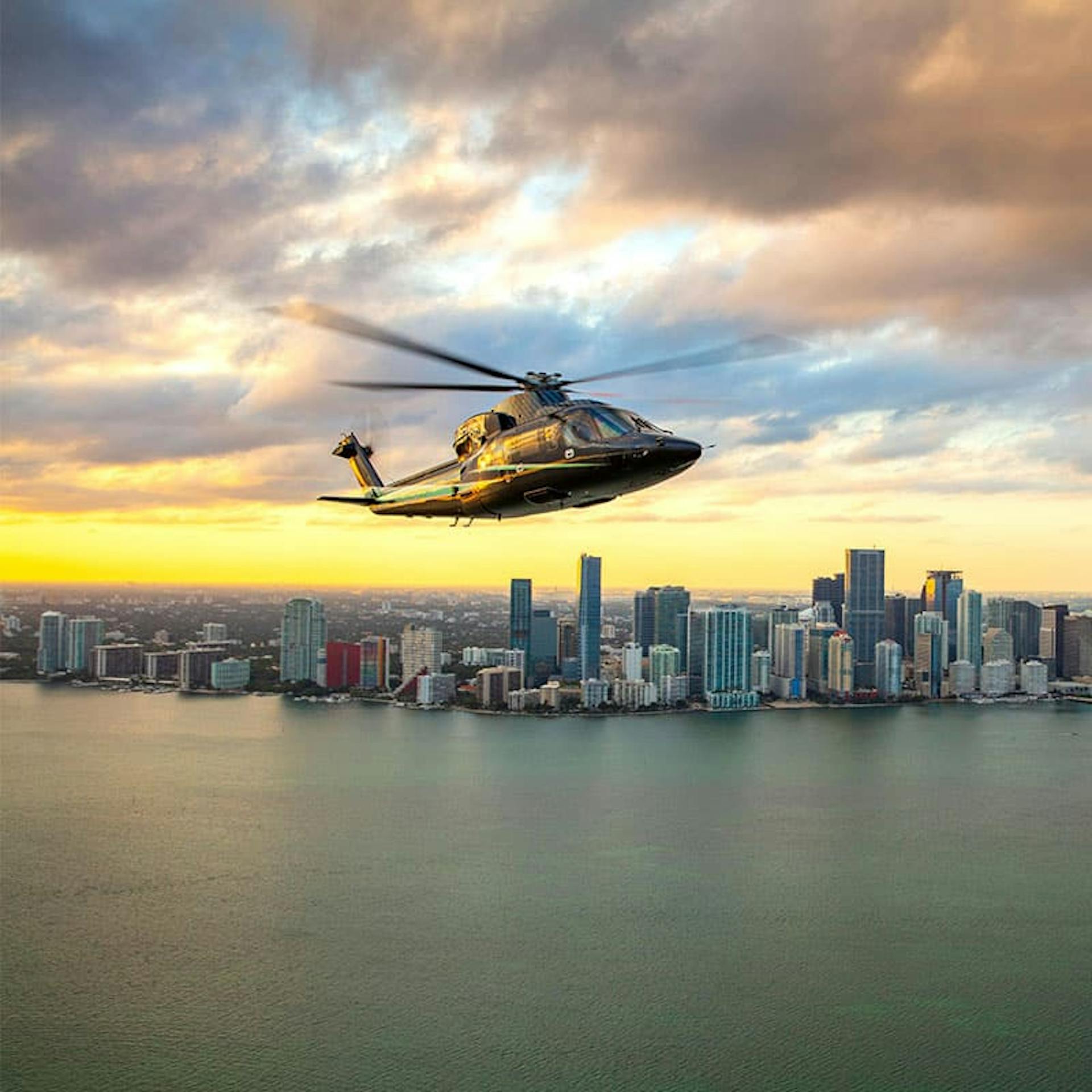 Helicopter flies over water reaching up to a city with skyscrapers and tall buildings reaching the edge of that water
