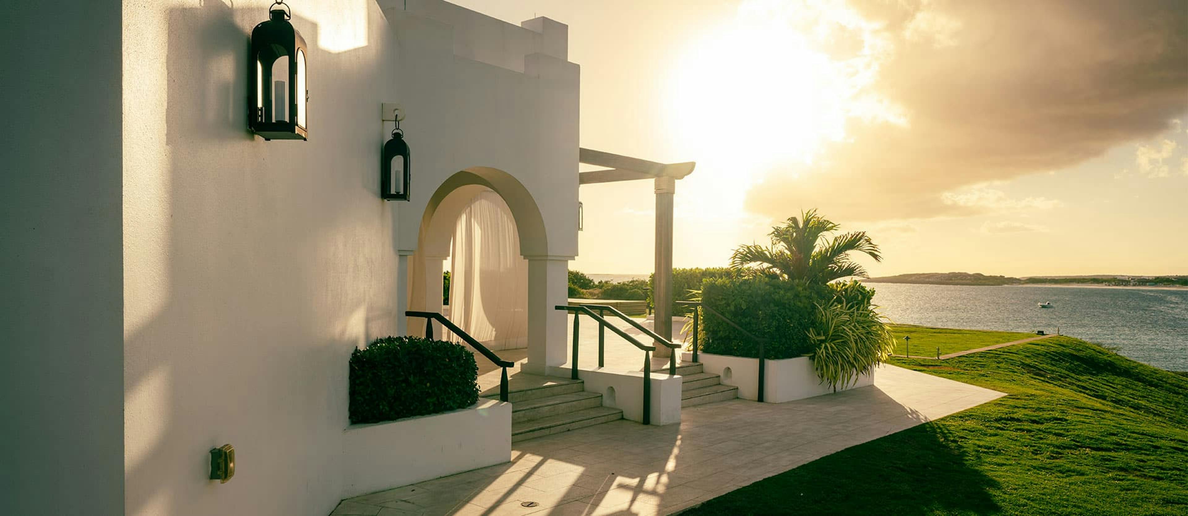 The white exterior of a building with a view of water and sunset
