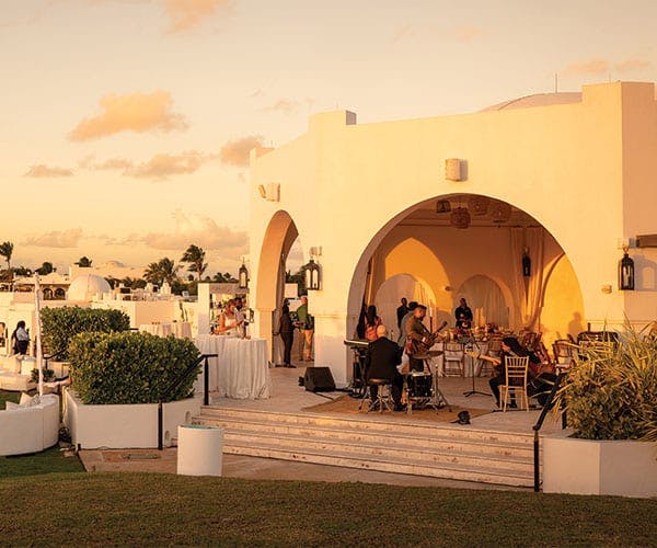 A band is set up outside with tables and white sofas for an event at a fancy location