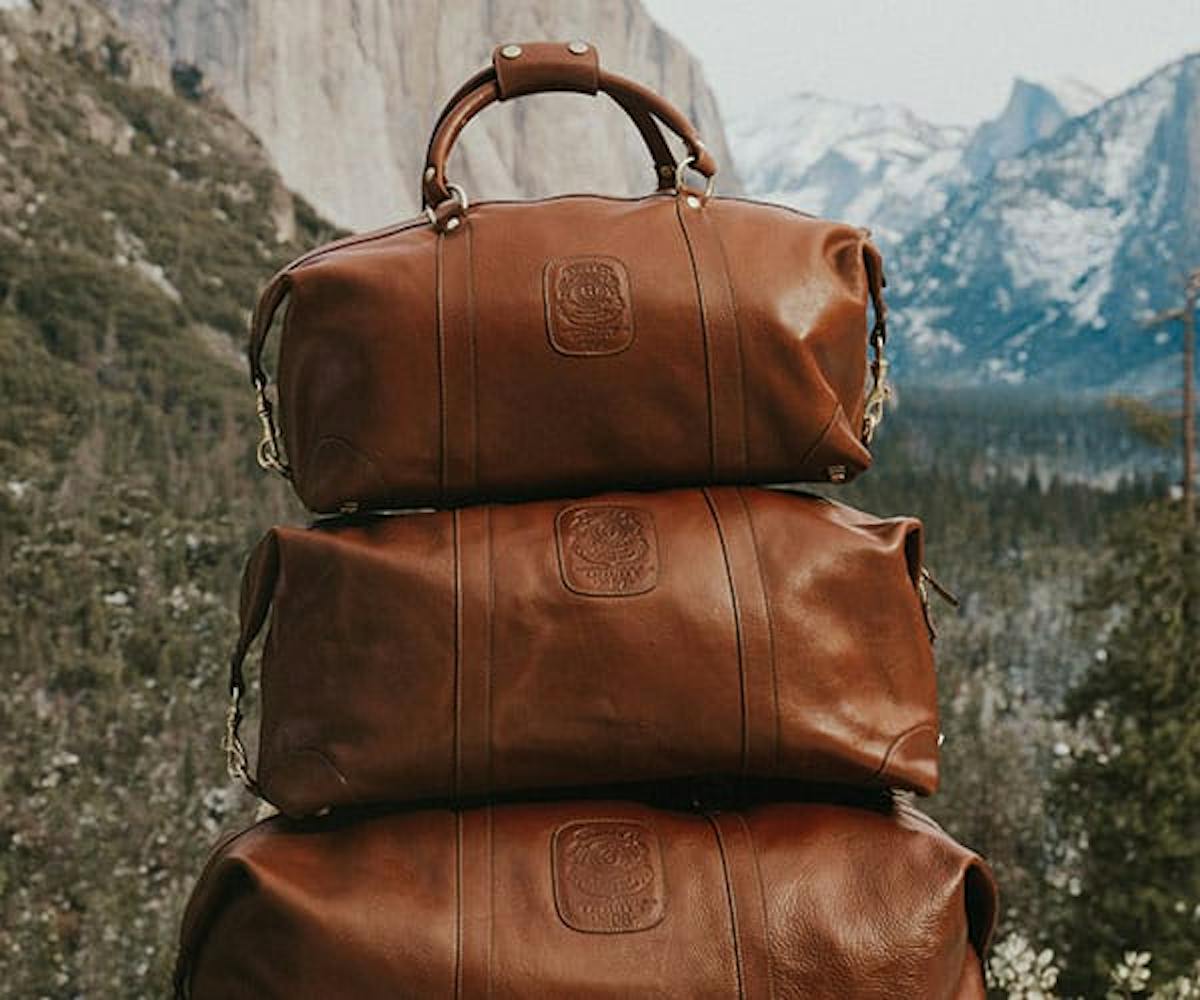 Three luxury travel bags of a brown leather variety stacked on top of one another, smallest down to largest